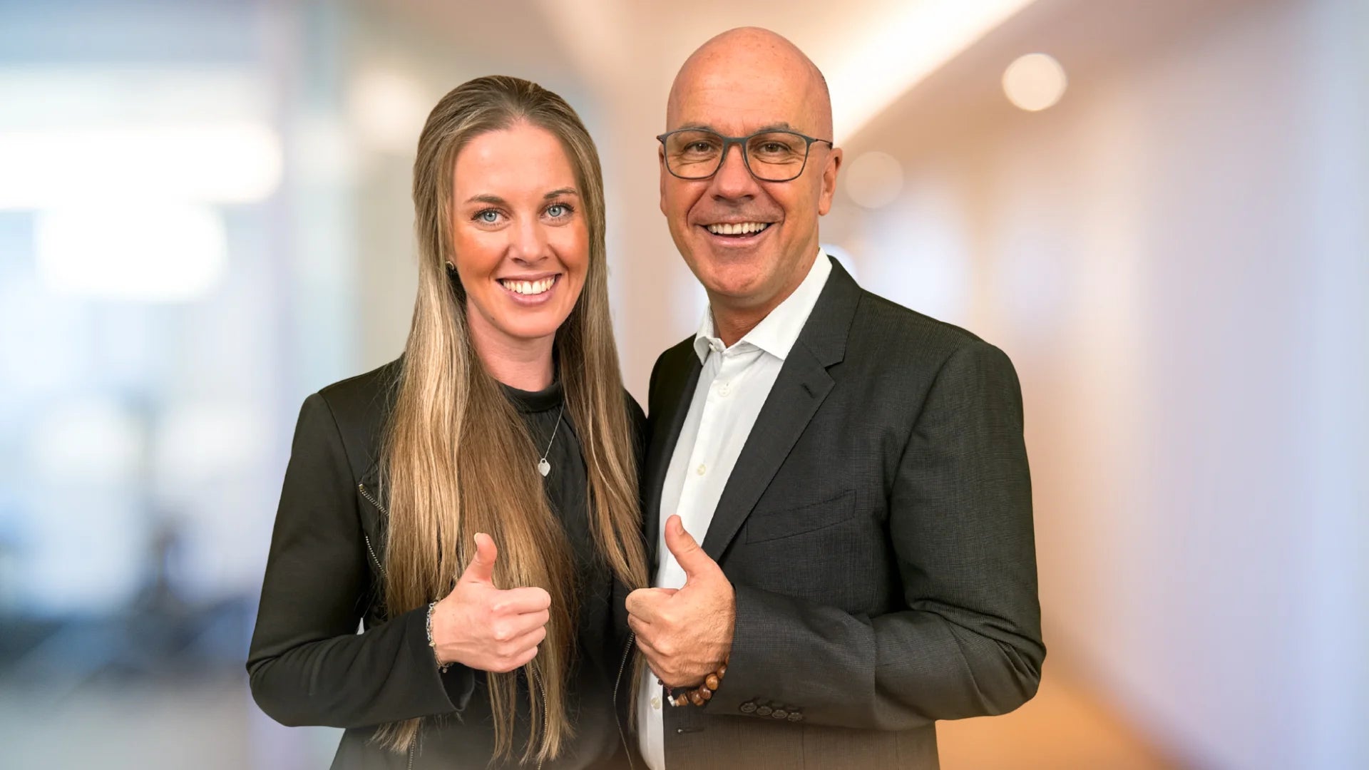 Alina und Marc Klejbor mit Daumen hoch vor modernem Büro Hintergrund, sympathisches Key Visual der Erfolgsimpulse GmbH für wirksame Unternehmensführung, Zusammenarbeit und digitale Systeme.
