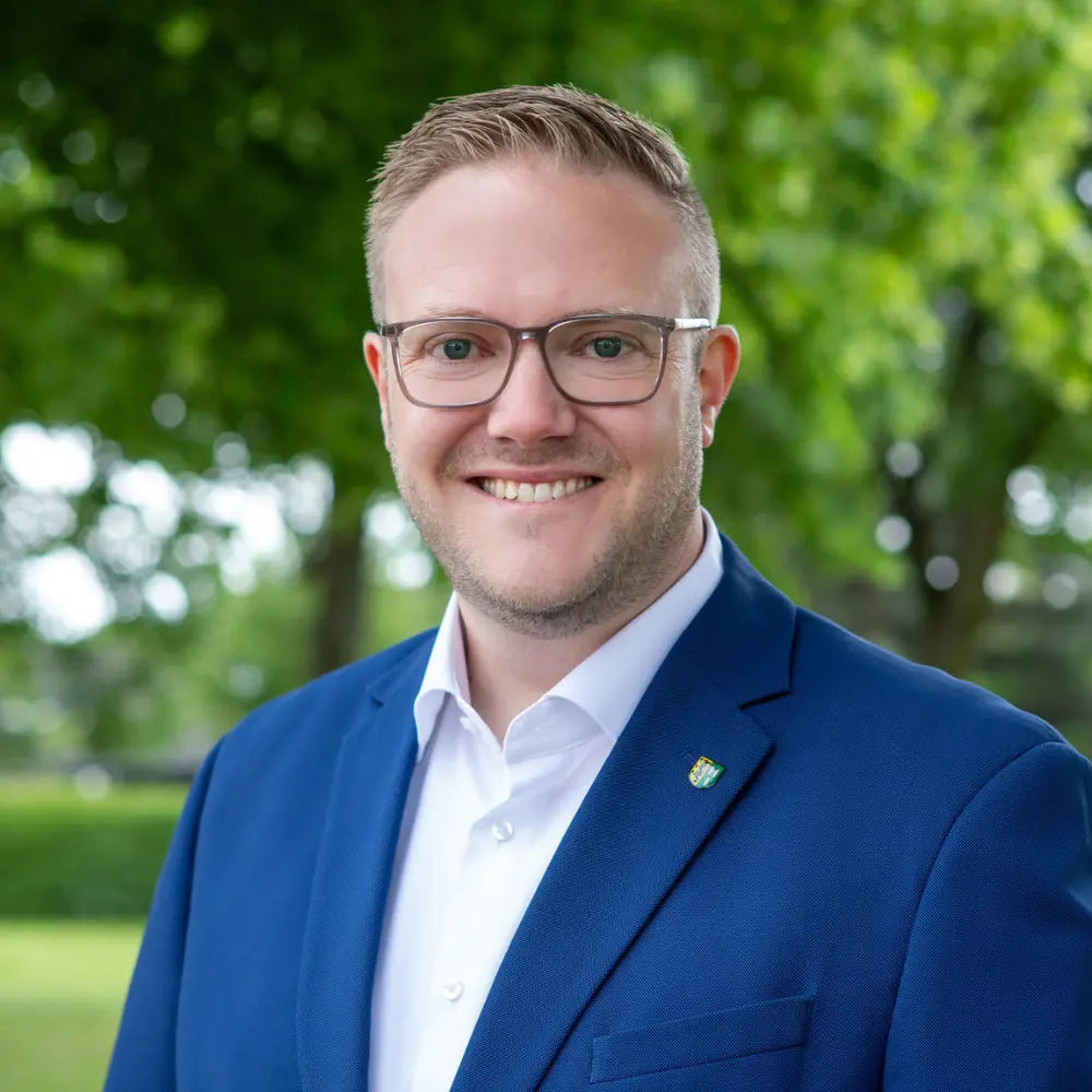 Porträt von Bürgermeister Moritz Pelzer im Anzug, vor grünem Hintergrund im Freien.