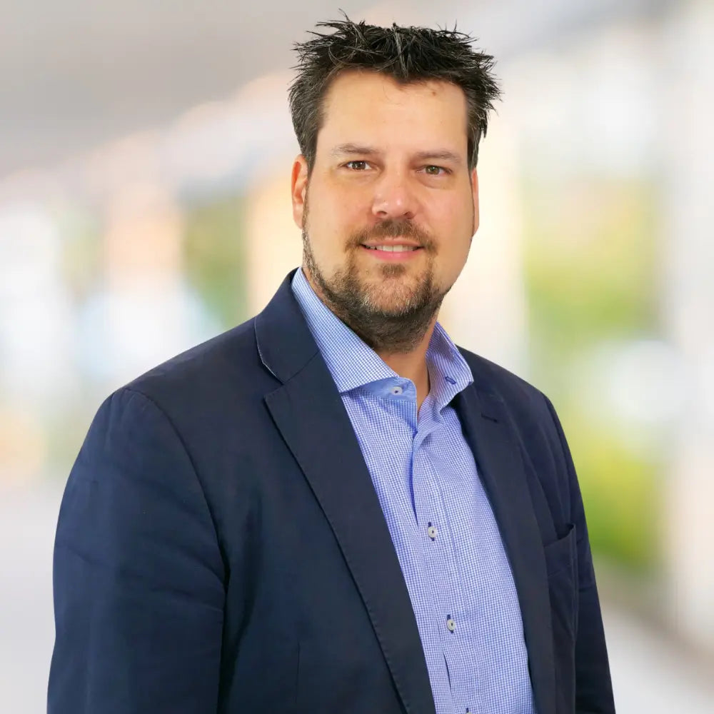 Porträt von Daniel A. Koczyba, Geschäftsführer, im Business Outfit vor modernem Hintergrund.