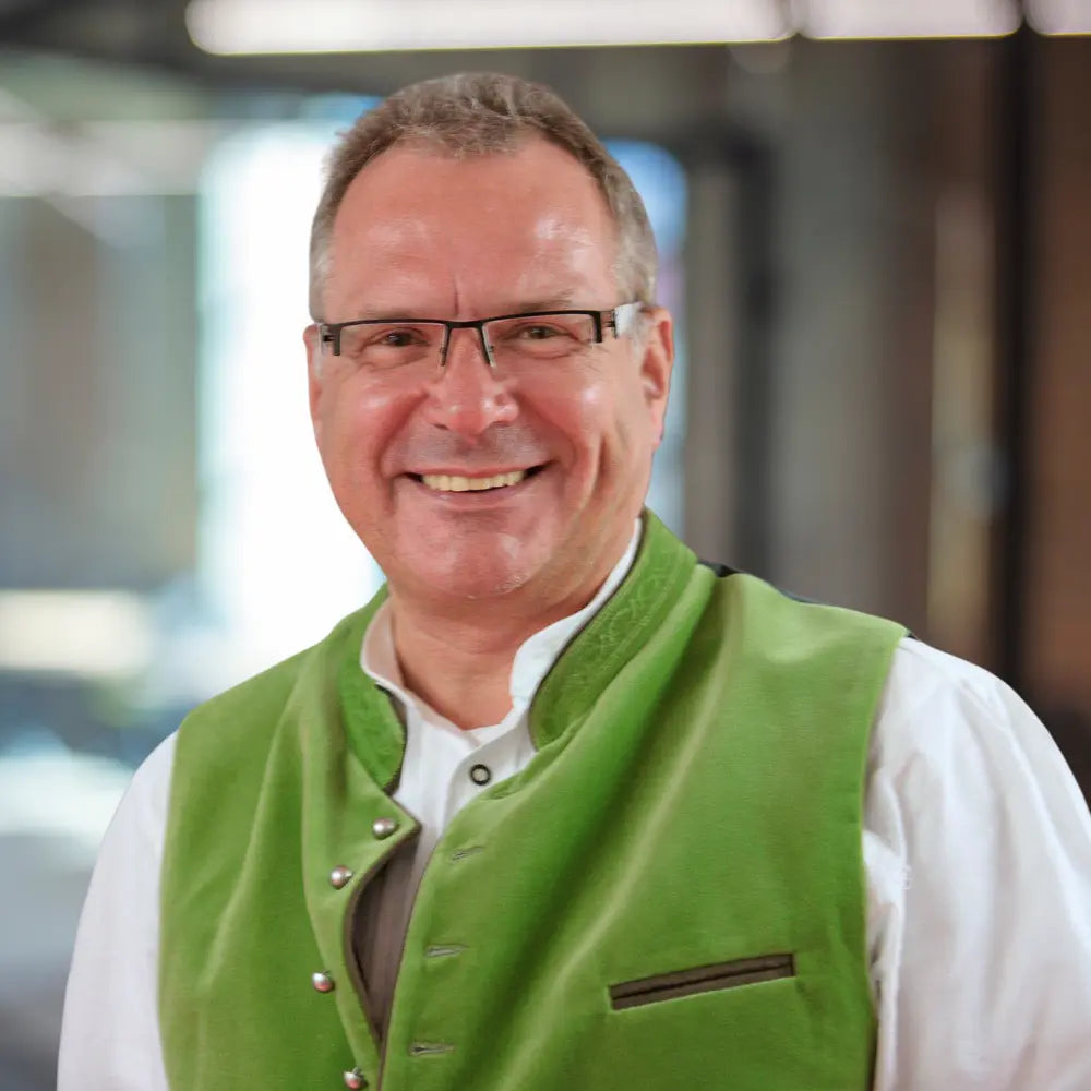 Porträt von Franz Josef Gomolka, Unternehmensberater, im Trachten Look mit grüner Weste vor modernem Hintergrund.