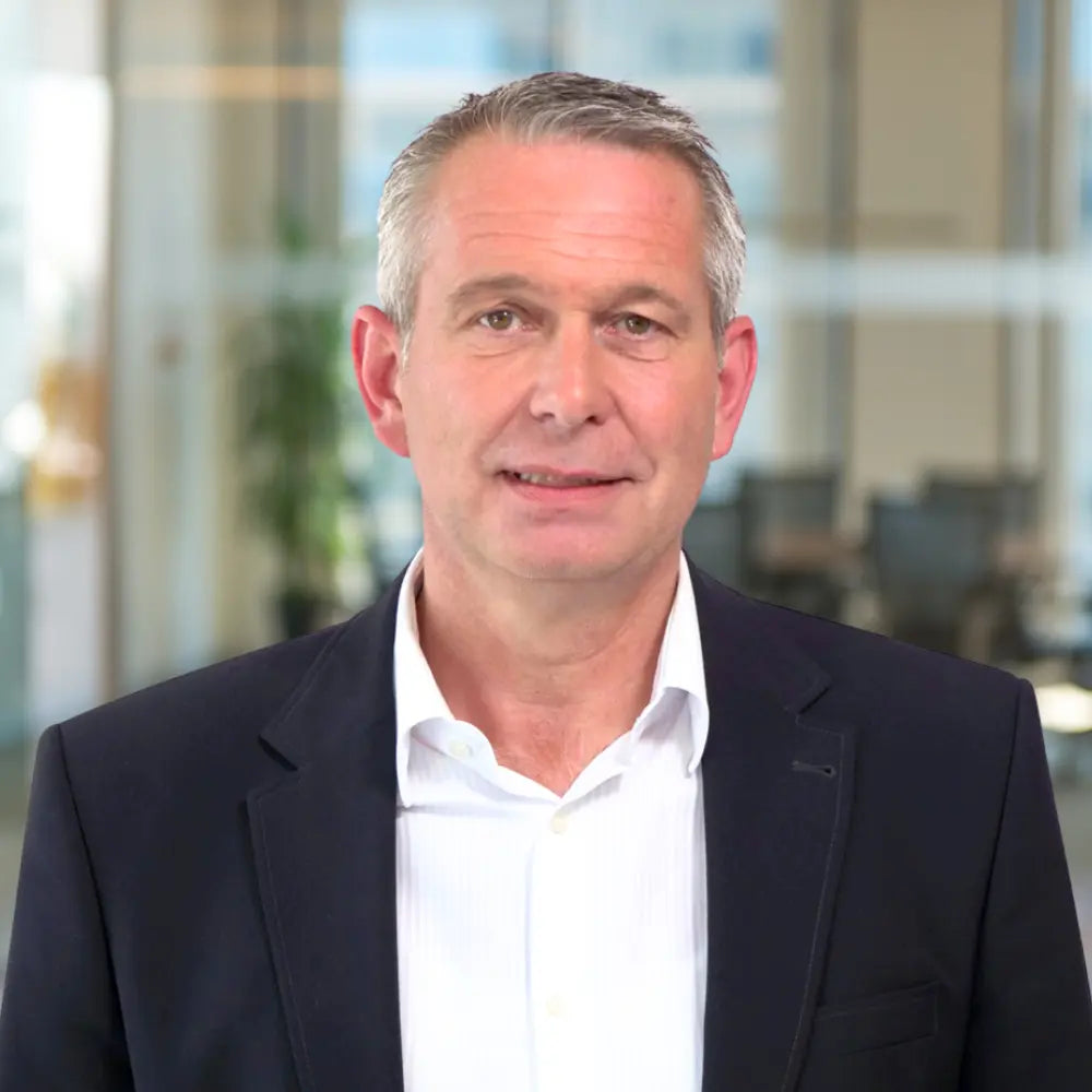 Porträt von Stephan Debey, Prokurist, im Anzug vor modernem Büro Hintergrund.