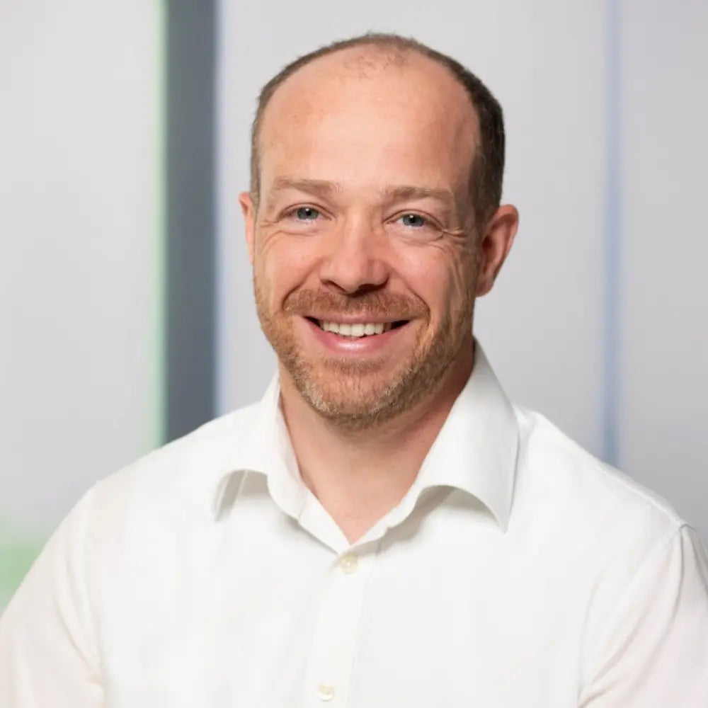 Business Porträt von Daniel Baum im weißen Hemd, freundlich lächelnd vor hellem Hintergrund, als Referenzmotiv für Leadership, Unternehmertum, Management und professionelle Unternehmenskommunikation.