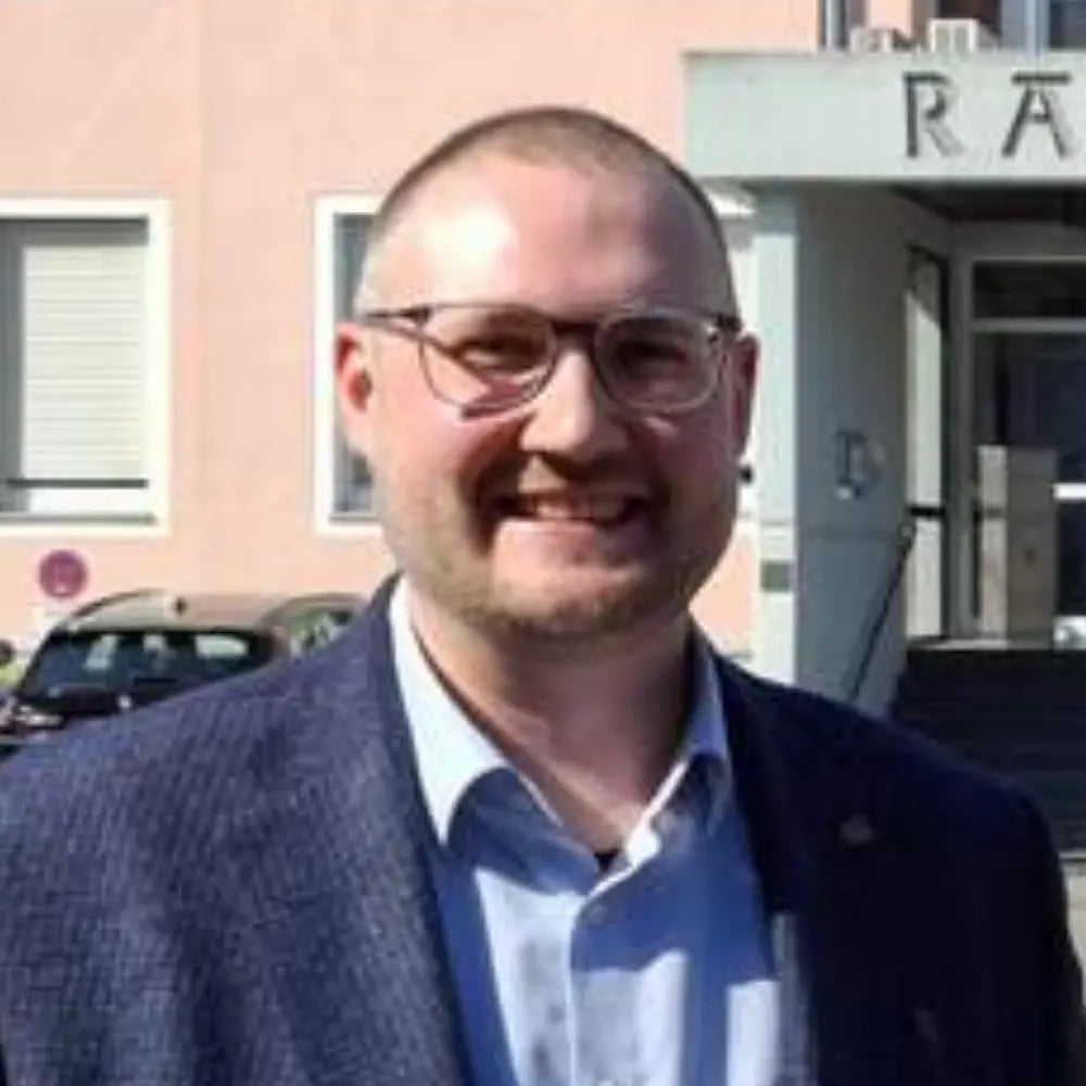 Business Porträt von Sven Cramer im blauen Sakko und hellblauen Hemd, freundlich lächelnd vor einem Gebäude, als Referenzmotiv für Unternehmertum, Management, Business Netzwerk und professionelle Unternehmenskommunikation.