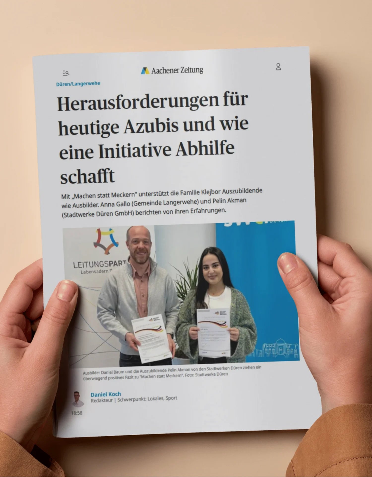 Mockup eines Artikels der Aachener Zeitung in zwei Händen, mit Überschrift zu den Herausforderungen heutiger Azubis und der Initiative Machen statt Meckern, ergänzt durch ein Foto mit zwei Personen und Dokumenten als Beispiel für mediale Berichterstattung über Ausbildungsförderung und gesellschaftliches Engagement.