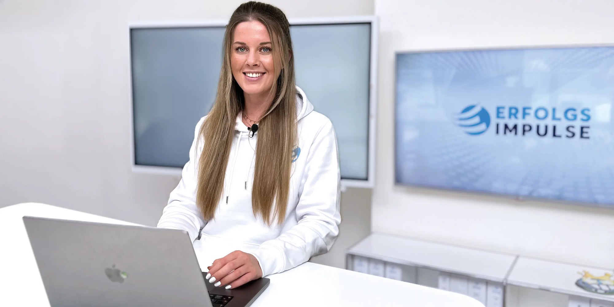 Alina Klejbor am Laptop im Studio der Erfolgsimpulse GmbH, im Hintergrund Monitor mit Erfolgsimpulse Logo, digitale Beratung und Online Training.