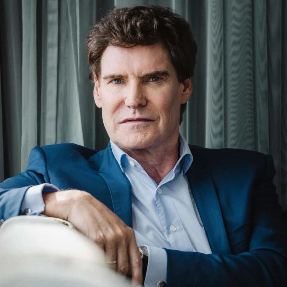 Carsten Maschmeyer in einem professionellen Business Porträt im blauen Anzug, sitzend in elegantem Innenraum vor grauen Vorhängen, für Unternehmerprofil, Leadership, Business Branding und persönliche Markenkommunikation.