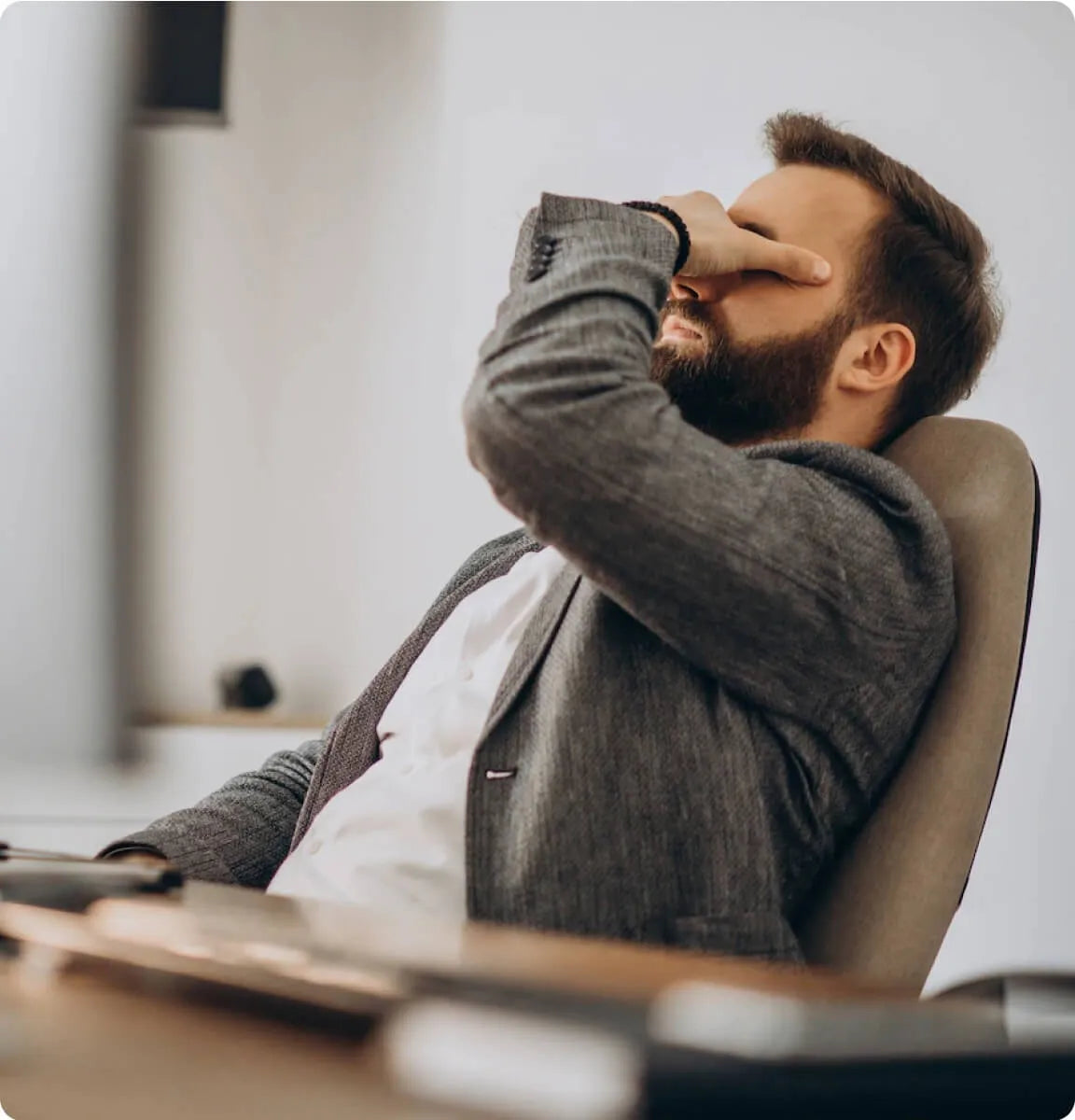 Erschöpfter Mitarbeiter im Büro mit Hand vor dem Gesicht, Symbolbild für Überlastung, Frustration und fehlende Wirksamkeit im Arbeitsalltag von Unternehmen.