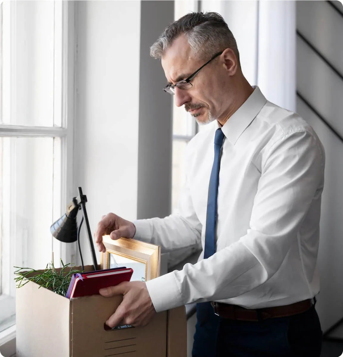 Mitarbeiter räumt seinen Arbeitsplatz und packt persönliche Gegenstände in einen Karton, Symbolbild für Kündigung, Mitarbeiterverlust und Fluktuation im Unternehmen.